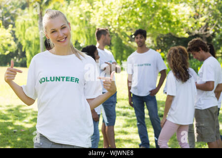 Schönen weiblichen Freiwilligen pointing at t-shirt mit Freunden im Hintergrund Stockfoto