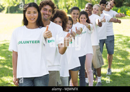 Portrait von zuversichtlich freiwillige Gestik Daumen hoch beim Stehen in einer Linie im Park Stockfoto