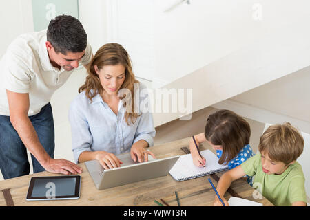 Hohe Betrachtungswinkel von Eltern mit Laptop, während die Kinder ausmalen am Tisch im Haus Stockfoto