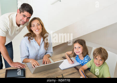 Hohen winkel Portrait von Kindern Färbung, während die Eltern mit Laptop zu Hause Stockfoto