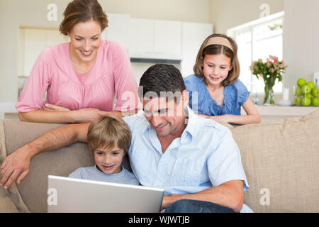 Vater mit Junge mit Laptop, während Mädchen und Mutter beobachten Sie im Wohnzimmer Stockfoto
