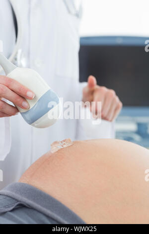 Mittelteil der Arzt mittels Ultraschall auf dem Bauch der schwangeren Frau in Klinik Stockfoto