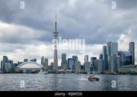 Blick vom Hafen von Toronto, Blick zurück auf die Skyline der Stadt an einem bewölkten Tag. Ein Wassertaxi überquert. Stockfoto