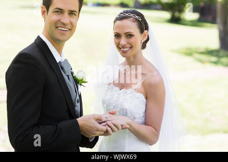 Portrait der junge Bräutigam Bräute platzieren Ring am Finger am Tag ihrer Hochzeit im Park Stockfoto