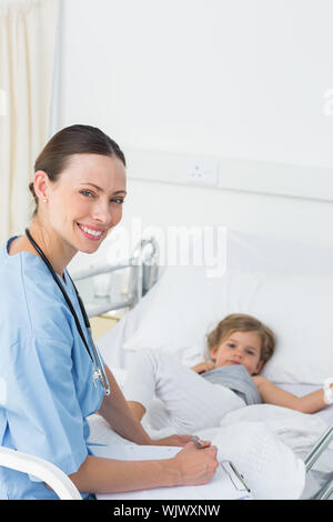 Portrait von lächelnden Frau Doktor mit Zwischenablage an Kranken Mädchen im Krankenhaus Stockfoto
