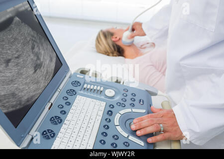 Männlicher Arzt mit sonogramm am Hals der weiblichen Patienten im Untersuchungsraum Stockfoto