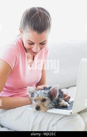 Hübsche Frau mit Laptop mit ihren Yorkshire Terrier zu Hause im Wohnzimmer Stockfoto