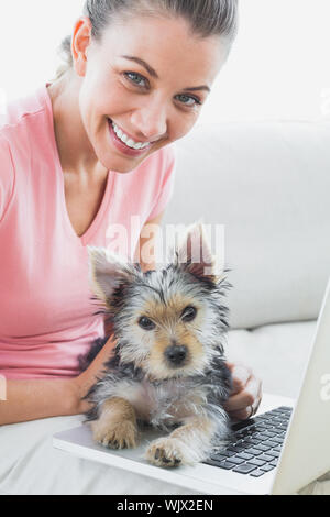 Fröhliche Frau mit Laptop mit ihren Yorkshire Terrier zu Hause im Wohnzimmer Stockfoto
