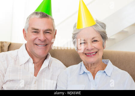 Senior Paar sitzt auf der Couch tragen Parteihüte zu Hause im Wohnzimmer Stockfoto