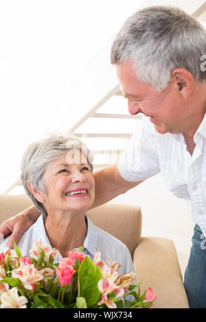 Älterer Mann, der seinem Partner einen Strauß Blumen zu Hause im Wohnzimmer Stockfoto