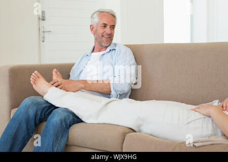 Liebevolle Mann, der seinem Partner einen Fuß Reiben auf der Couch zu Hause im Wohnzimmer Stockfoto