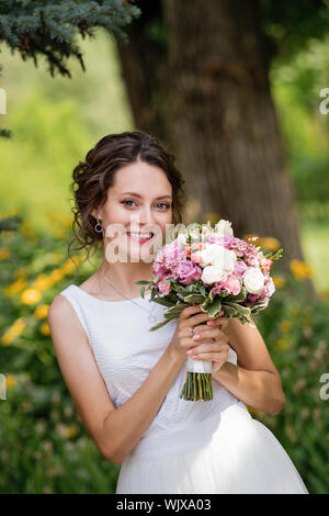 Emotionale Portrait von einer glücklichen Braut in der Mode Hochzeit Kleid auf die natürlichen Hintergrund. Frisch Verheiratete mit einem brautstrauß in der Hand lacht glücklich nach t Stockfoto