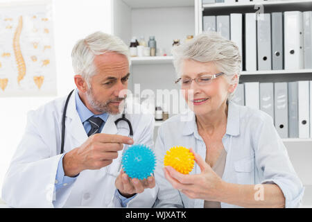 Männlicher Arzt zeigt Stress Buster Kugeln zu den älteren Patienten am medizinischen Büro Stockfoto