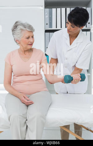 Weibliche Physiotherapeut Unterstützung der älteren Frau, die Hantel in die Arztpraxis zu heben Stockfoto