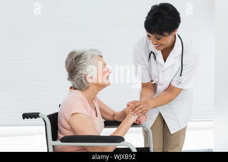 Ärztin sprechen zu einem älteren Patienten im Rollstuhl im Krankenhaus Stockfoto