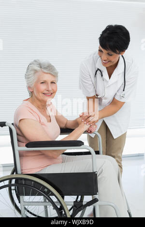 Ärztin sprechen zu einem älteren Patienten im Rollstuhl im Krankenhaus Stockfoto