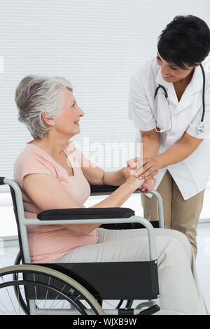 Ärztin sprechen zu einem älteren Patienten im Rollstuhl im Krankenhaus Stockfoto