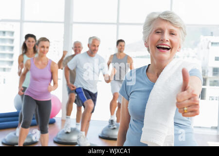 Freundliche ältere Frau Gestik Daumen hoch mit Menschen trainieren in den Hintergrund Fitness Studio Stockfoto