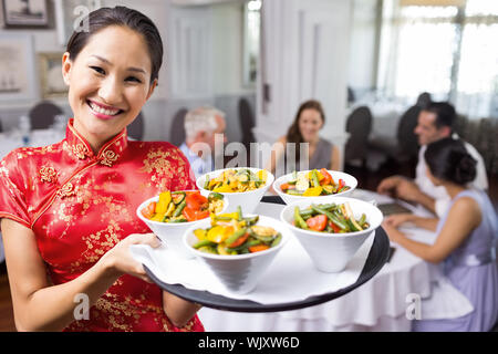 Porträt einer Kellnerin mit Lebensmitteln Fach mit Menschen am Esstisch im Restaurant sitzen Stockfoto