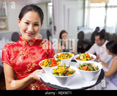 Porträt einer Kellnerin mit Lebensmitteln Fach mit Menschen am Esstisch im Restaurant sitzen Stockfoto