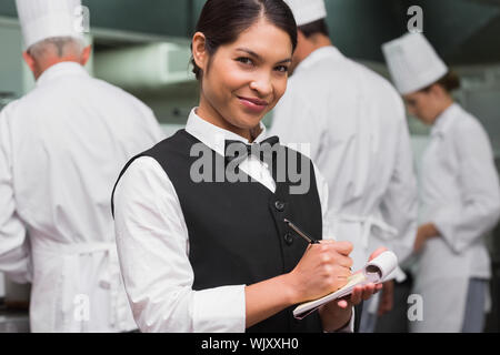 Happy Kellnerin schreiben auf Pad in einem kommerziellen Küche Stockfoto