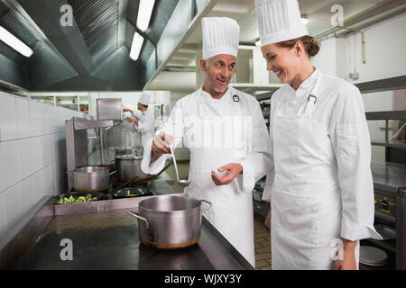 Zwei glückliche Köche über einen großen Topf auf dem Herd Chatten in einem kommerziellen Küche Stockfoto