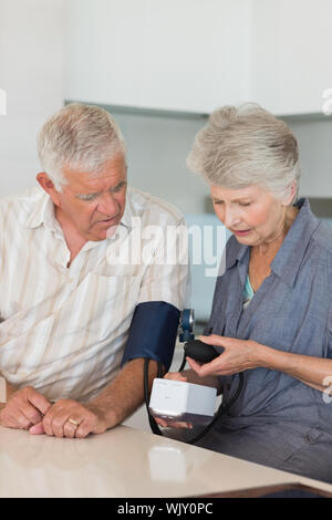 Ältere Frau ihre Ehemänner den Blutdruck zu Hause in der Küche Stockfoto