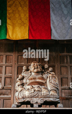 DEC 3, 2018 Yamagata, Japan - Japanische geschnitztem Holz lächelnden Buddha Statue unter bunten Buddhismus Flaggen Yamadera Risshaku ji Temple Stockfoto