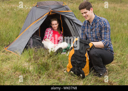 Glücklicher Mann Rucksack packen, während Freundin im Zelt sitzt Stockfoto