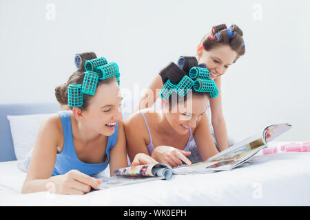 Mädchen tragen Schlafanzüge und Lockenwickler sitzen im Bett mit Zeitschriften Stockfoto