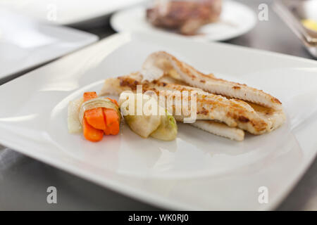 Gebratene Fischfilets und Gemüse garniert auf einer Platte in einem Restaurant mit Platz für Salat oder eine zusätzliche Portion Gemüse Stockfoto