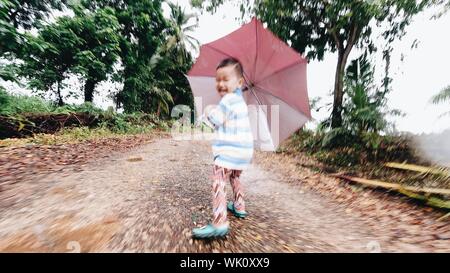 Der Junge war glücklich Verbreitung ein Regenschirm, glücklich lächelnd außerhalb Wandern. Stockfoto