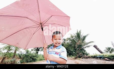 Der Junge war glücklich Verbreitung ein Regenschirm, glücklich lächelnd außerhalb Wandern. Stockfoto