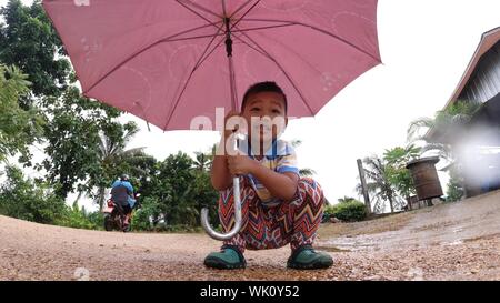 Der Junge war glücklich Verbreitung ein Regenschirm, glücklich lächelnd außerhalb Wandern. Stockfoto