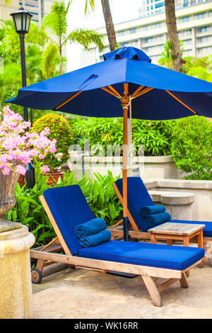 Zwei blaue Liegestühle mit Sonnenschirmen in der Nähe von Schwimmbad im Luxushotel Stockfoto