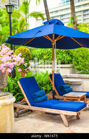 Zwei blaue Liegestühle mit Sonnenschirmen in der Nähe von Schwimmbad im Luxushotel Stockfoto