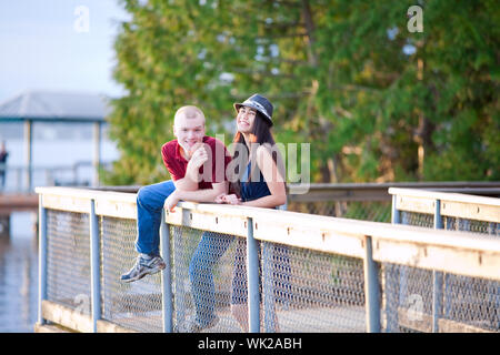 Junge glückliche interracial paar stehen zusammen auf Holzsteg mit Blick auf See, lachen Stockfoto