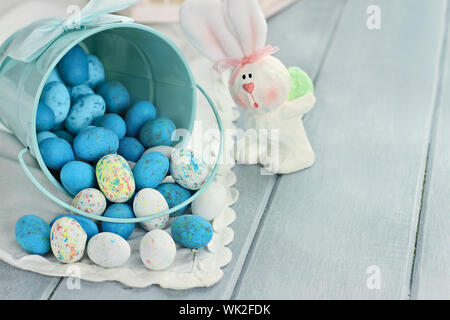 Eine blaue Blecheimer umgekippt, verschütten Süßigkeiten Ostereier auf einen Tisch. Geringe Schärfentiefe. Stockfoto