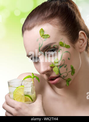 Schönheit-Porträt der niedliche Brünette Mädchen mit kreativen grüne Make-up und einige Minzeblätter auf dem Gesicht, nehmen einen cocktail Mojito in der hand Stockfoto