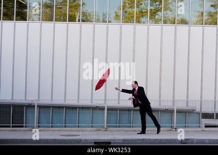 Asiatische Geschäftsmann festhalten an seinen Regenschirm an einem windigen Tag Stockfoto