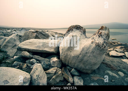 Riesige Felsbrocken im Vordergrund in der Steppe am See an einem nebligen Morgen. Große Steine gehäuft in Haufen. Getönt. Kopieren Sie Platz. Stockfoto