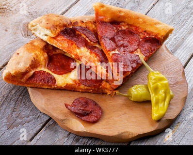 Scheiben der Leckere Pepperonipizza mit zwei jalapeno Pfeffer auf Holzplatte closeup auf rustikalen Holzmöbeln Hintergrund Stockfoto