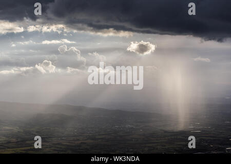 Sonnenstrahl scheint durch Wolken und Regen über die Berge in der Mitte der Schatten Stockfoto