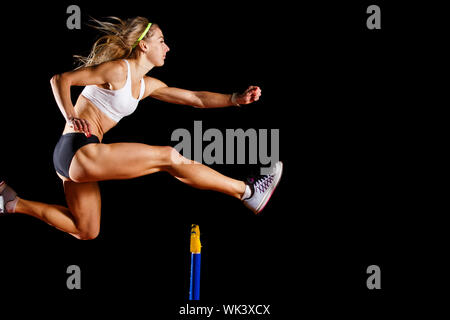 Muskulöse Sportlerin über Hürde auf Sprint Rennen auf schwarzem Hintergrund isoliert springen Stockfoto