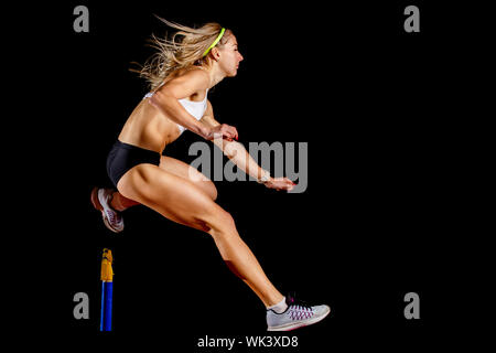 Muskulöse Sportlerin über Hürde auf Sprint Rennen auf schwarzem Hintergrund isoliert springen Stockfoto