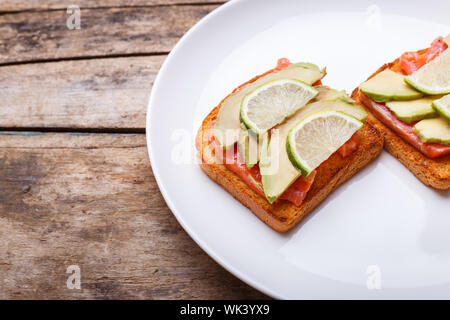 Frischer Lachs Sandwich mit Avocado und Kalk auf weiße Platte. Stockfoto