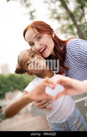 Rothaarige Frau mit hellen Lippen ihr lustig Tochter umarmen Stockfoto