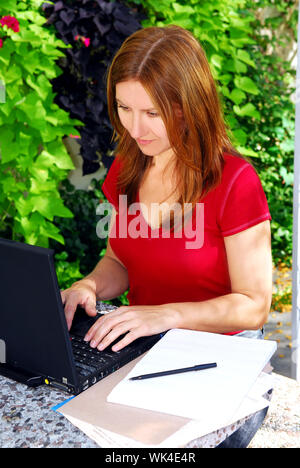 Reife Frau, die auf tragbaren Computer in ihrem Garten zu Hause arbeiten Stockfoto