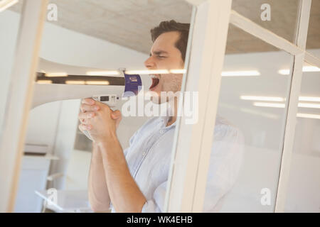 Casual Geschäftsmann Schreien über Megaphon in seinem Büro Stockfoto