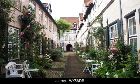 Lübeck, Deutschland - 07/26/2015 - schönen gemütlichen Innenhof mit weißen Bänke, Pflanzen und Blumen in der Straße der alten Stadt Stockfoto